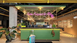 A hotel reception area with a neon sign, a reception desk, a green counter, and a 'Nice to see you' mat. - Moxy Budapest Downtown (Budapest)