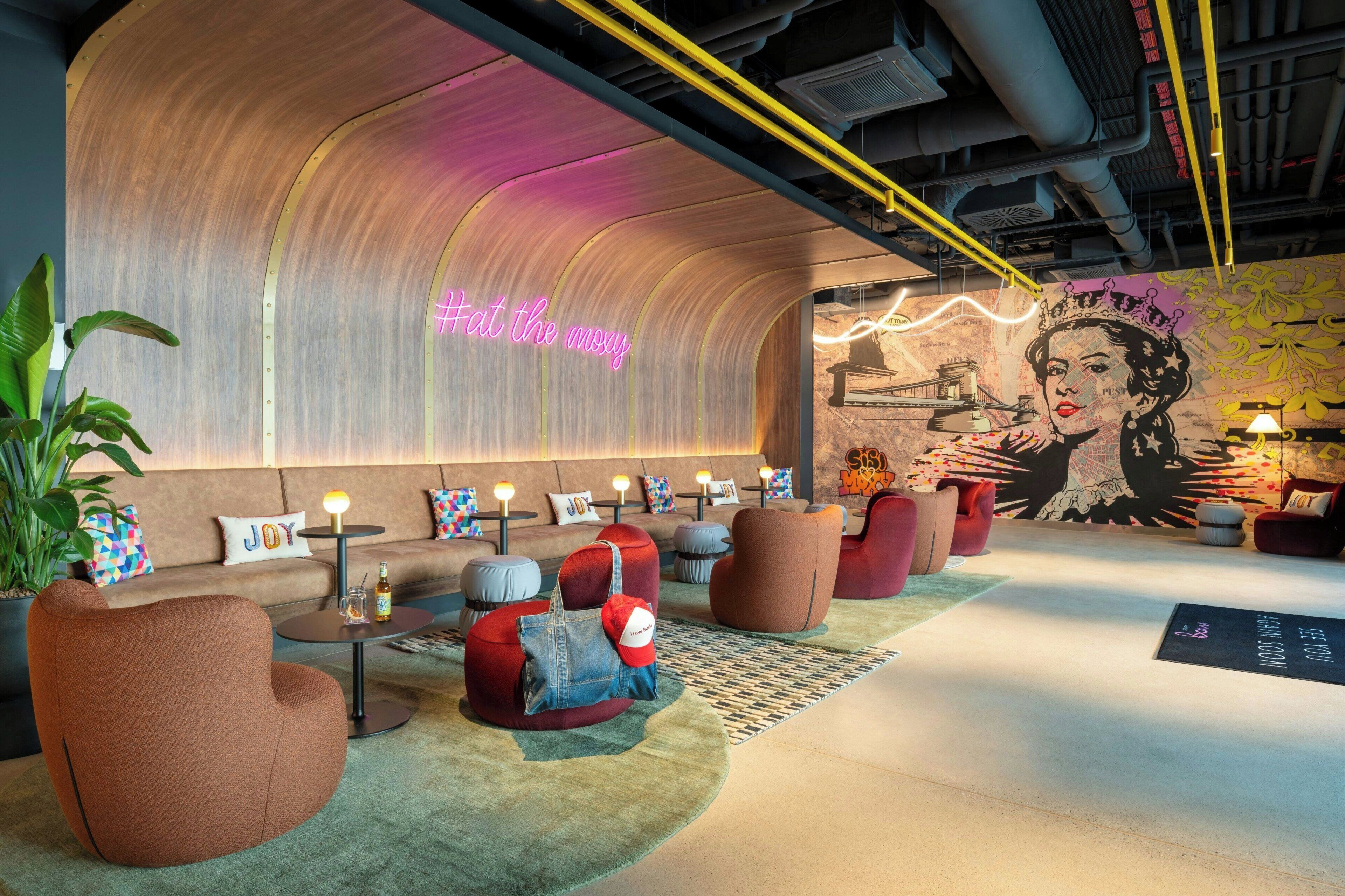 A modern lounge area with curved seating, neon signage, and a mural.