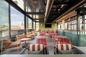 A rooftop bar with outdoor seating, a bar area, and a view of a cityscape. - Moxy Budapest Downtown (Budapest)