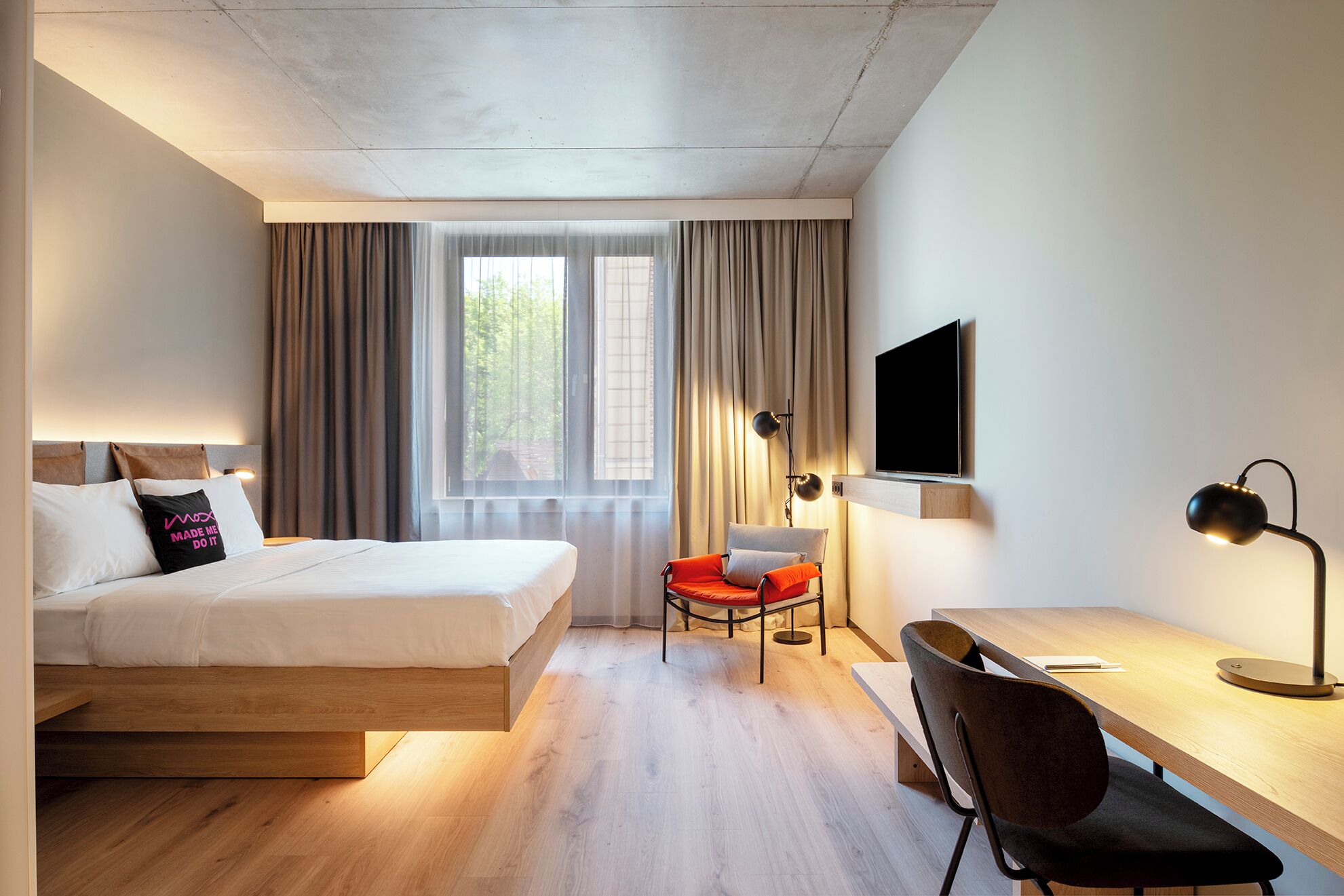 A hotel room with a bed, a desk, a chair, a TV, and a window with curtains.