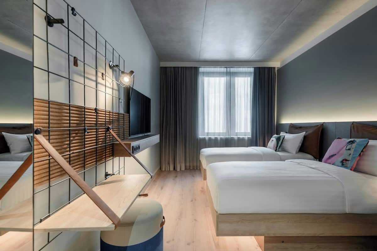 A modern hotel room with a large bed, a desk, a TV, and a window with curtains.