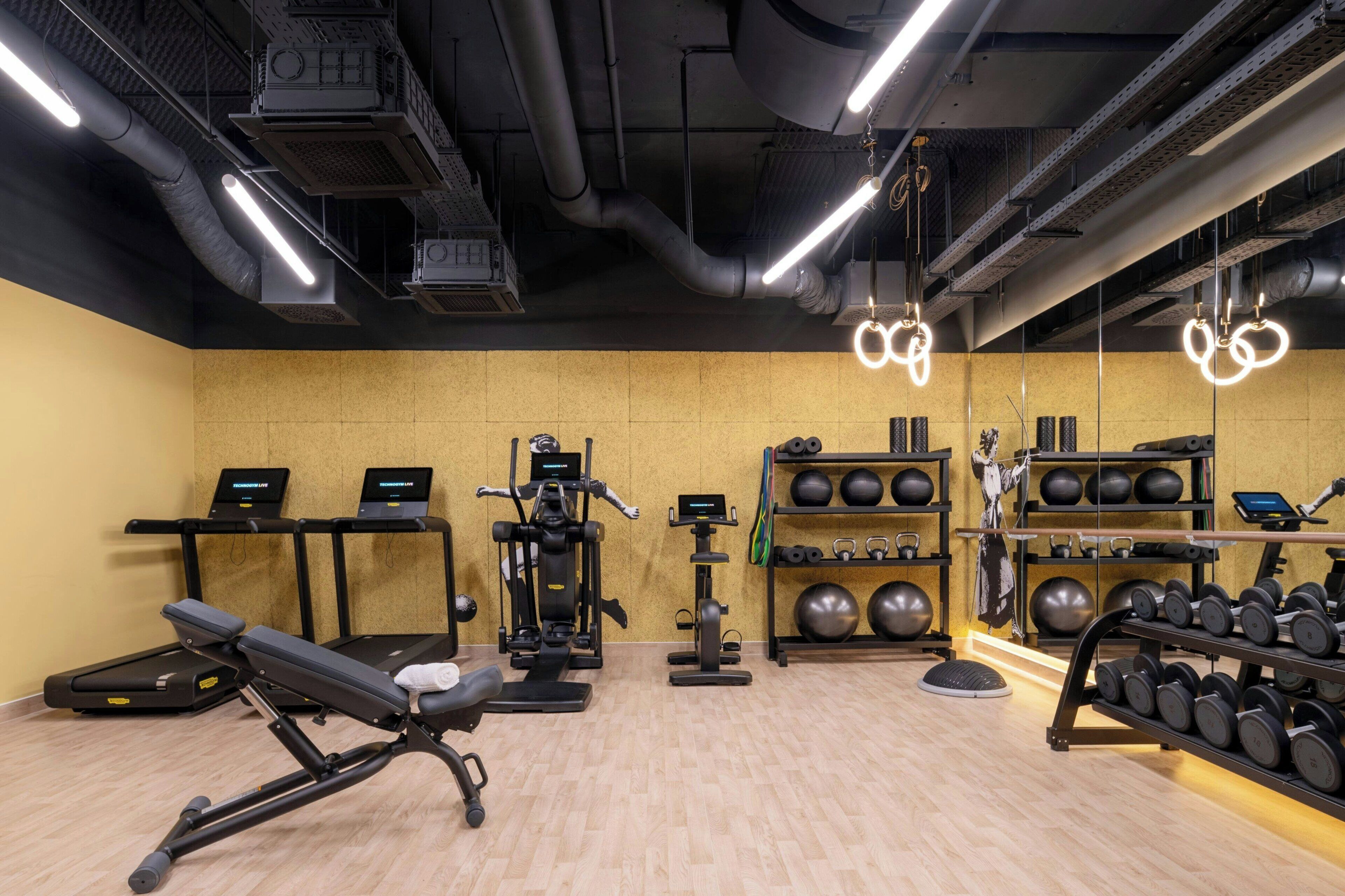 Un gimnasio con equipo de ejercicio, cintas de correr y un espejo instalado en la pared.