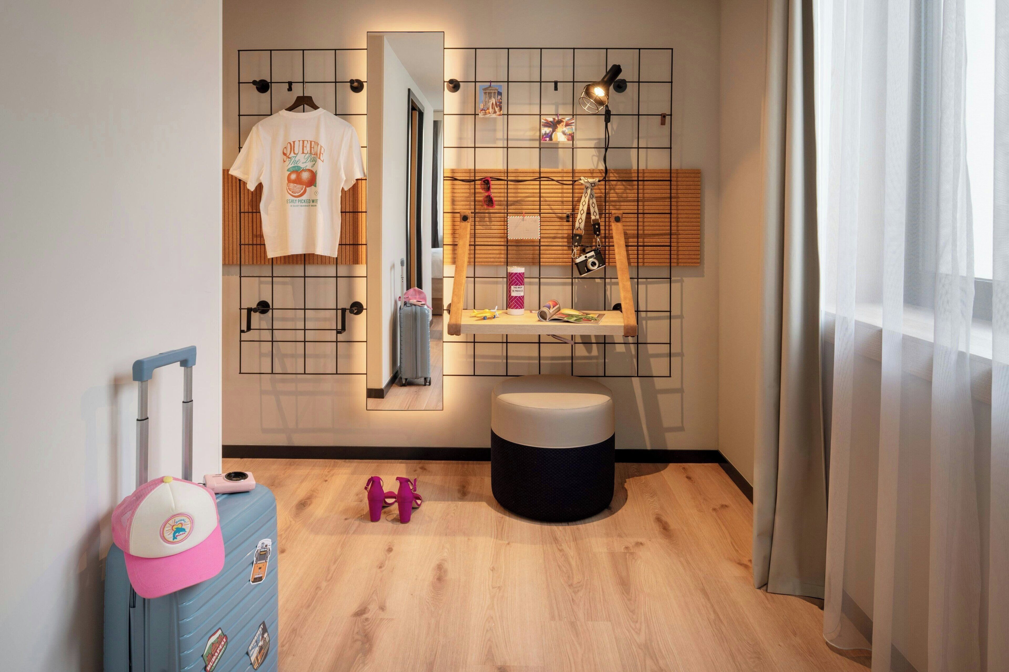 A modern bathroom with a wooden floor, a mirror with a grid pattern, a small stool, and a suitcase.