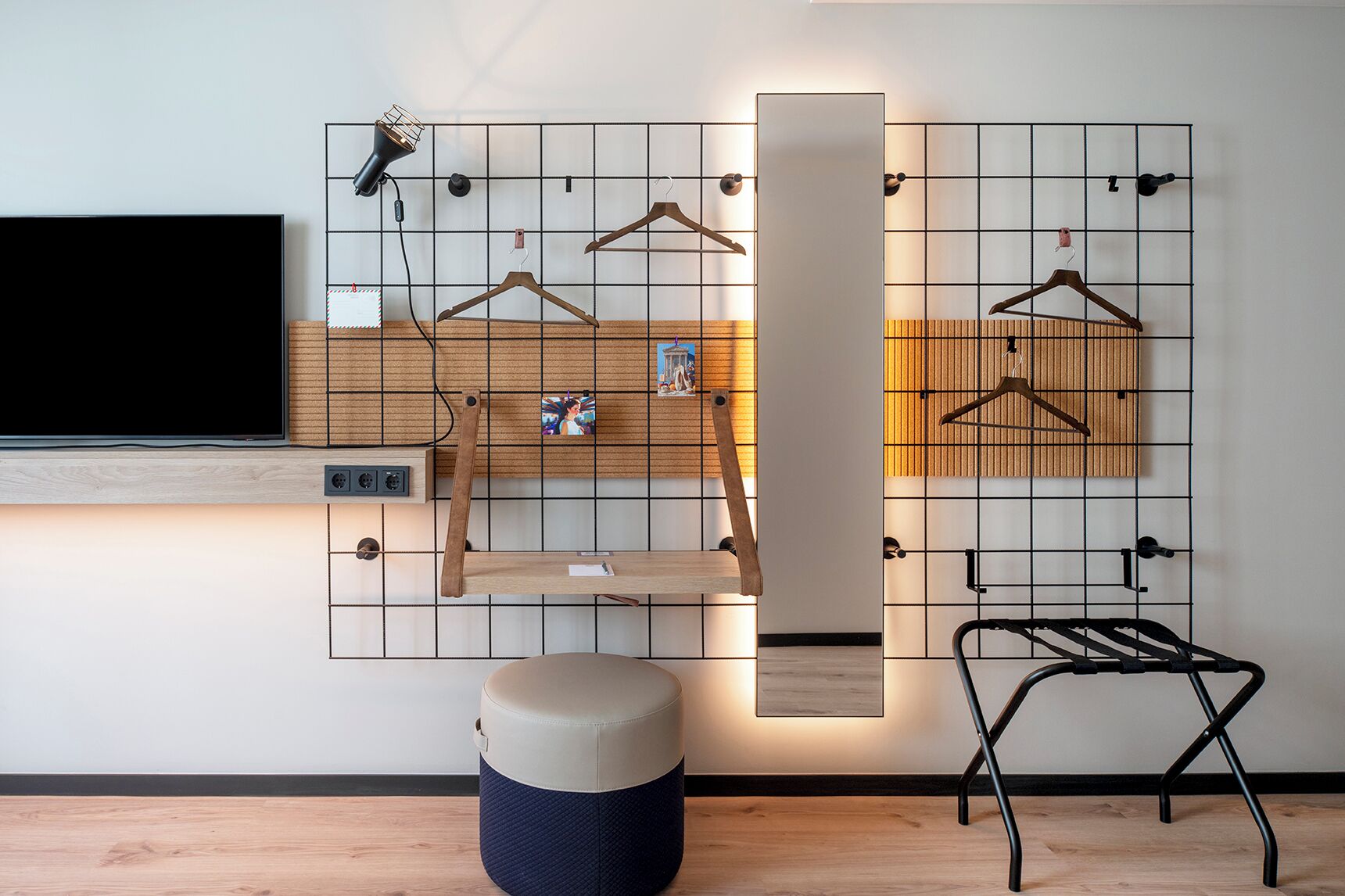 A modern room with a TV, a wooden shelf, a hanging light, a wall-mounted rack with hangers, a stool, and a laundry rack.