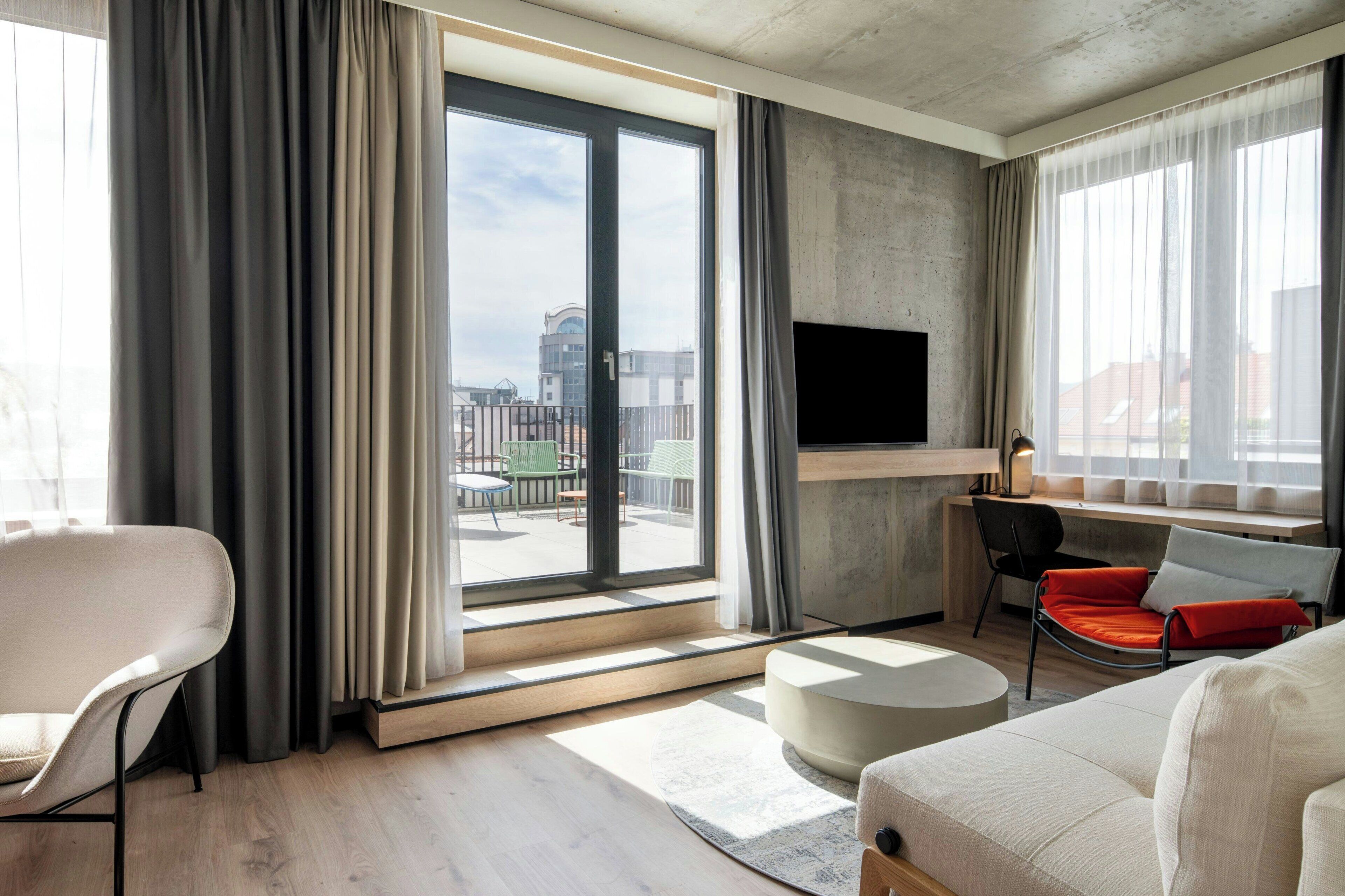Un salon moderne doté d’une grande fenêtre, d’un téléviseur à écran plat fixé au mur et d’un espace détente comprenant un canapé et des fauteuils.