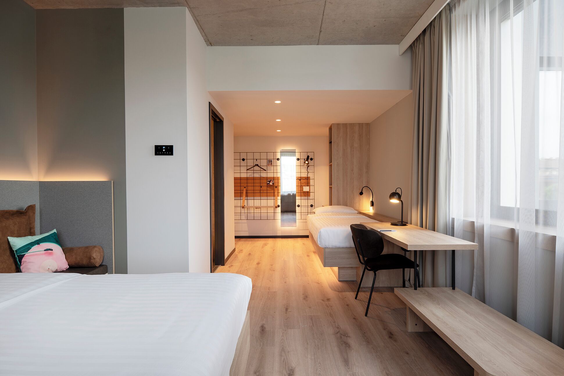 A modern hotel room with a bed, a desk, and a view of the city.