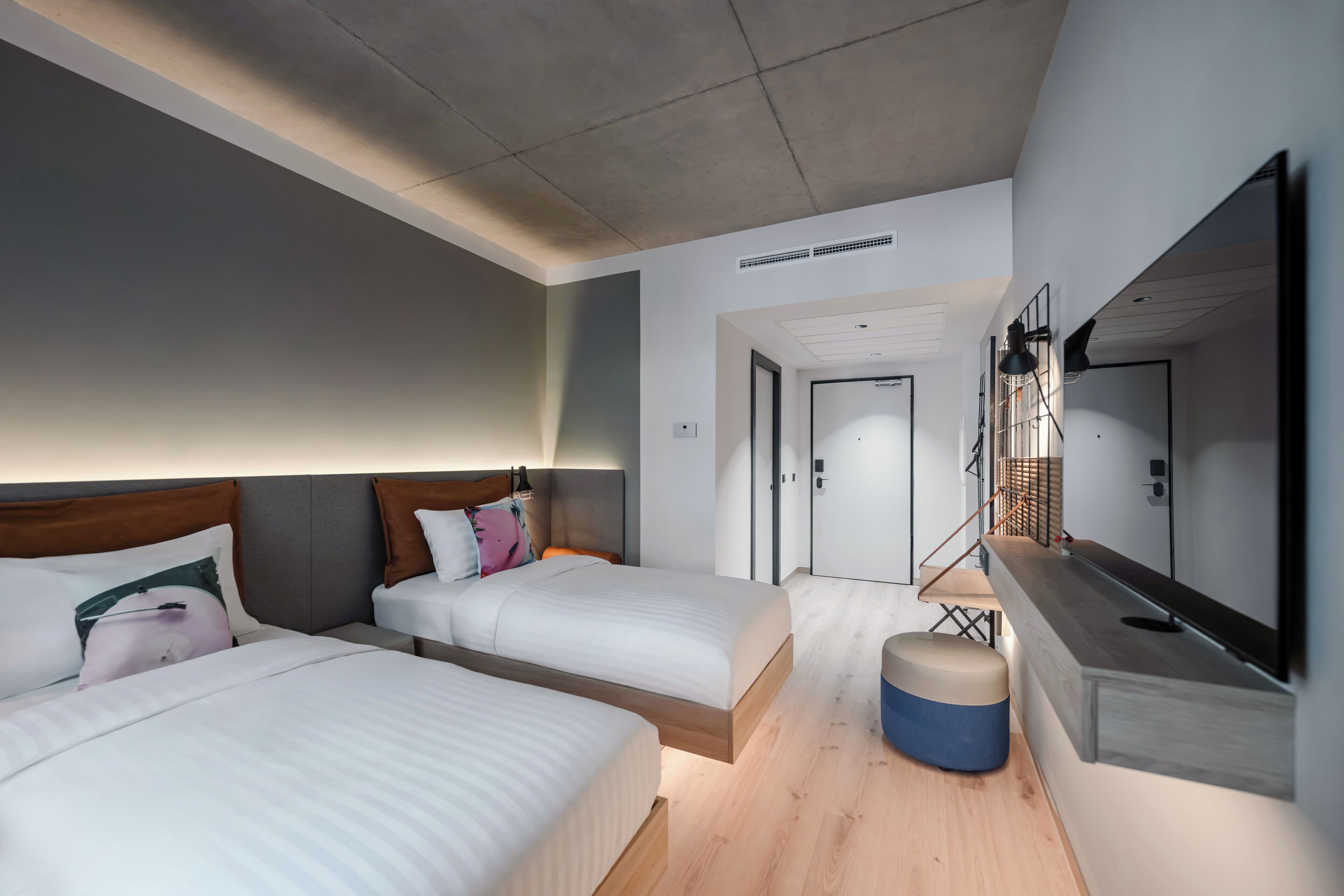 A modern hotel room with two beds, a small seating area, a large mirror, and a door leading to another room.