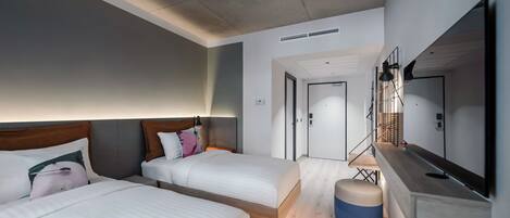 A modern hotel room with two beds, a small seating area, a large mirror, and a door leading to another room.