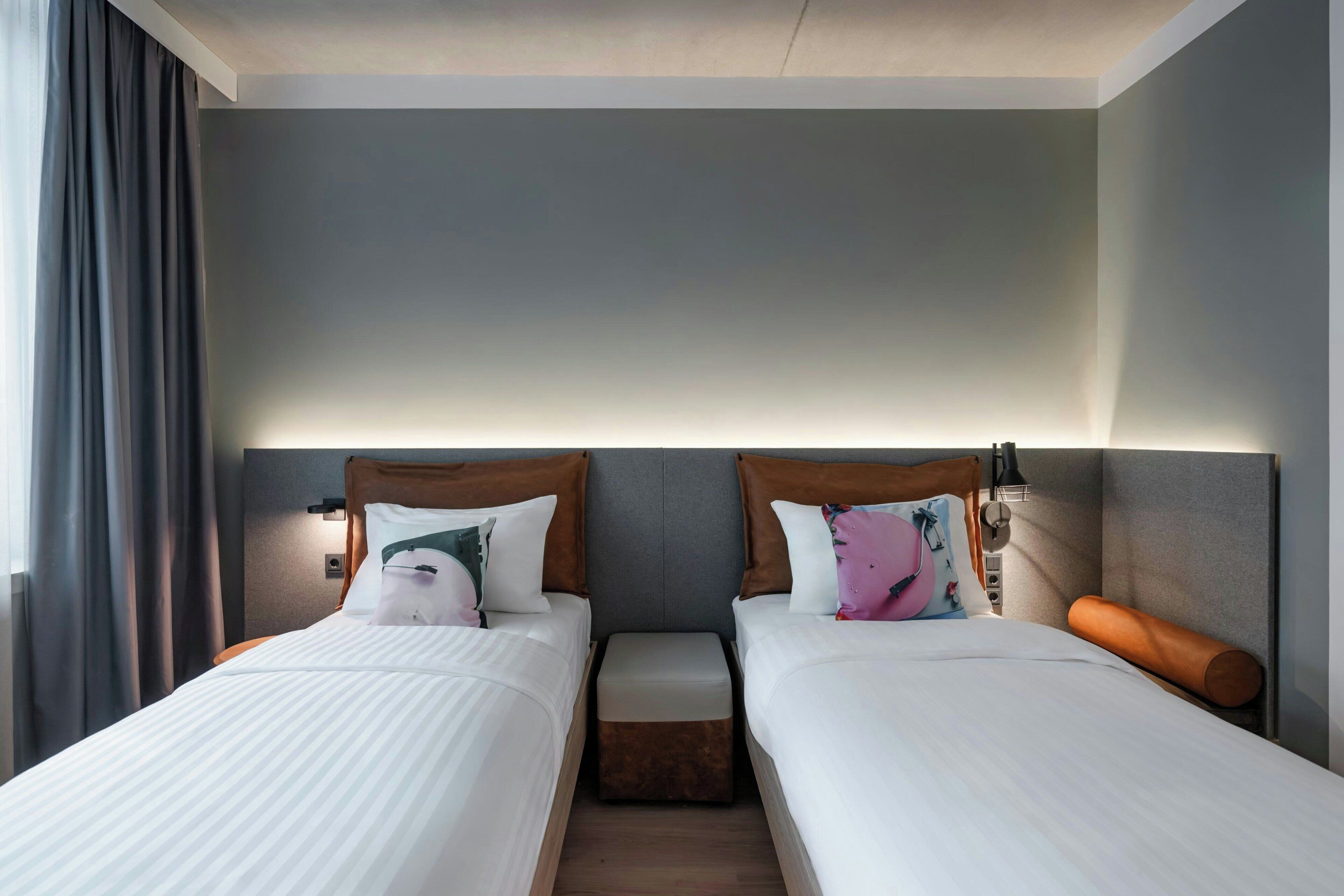 Habitación de hotel con dos camas, mesitas de noche y un ventanal con cortinas.