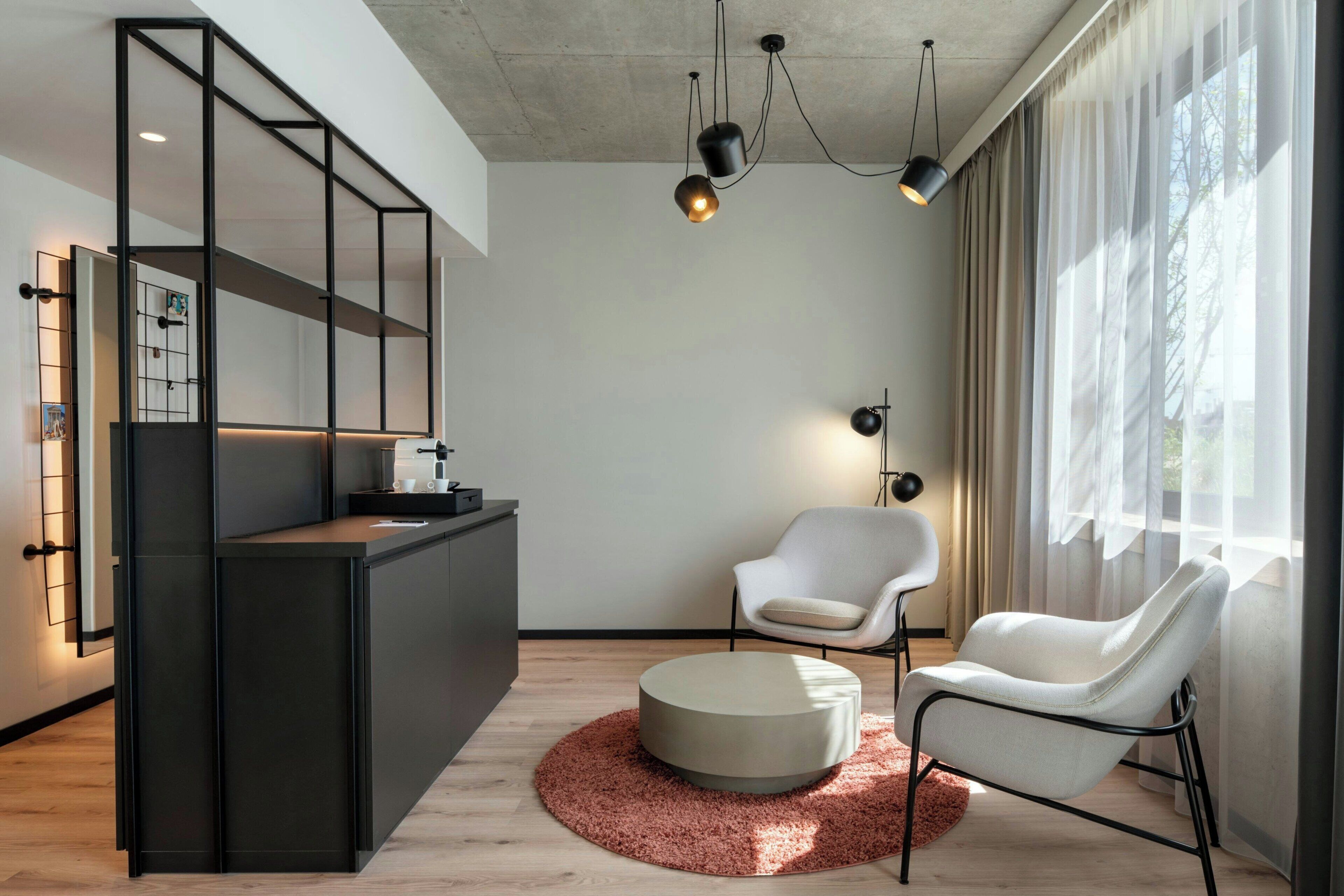 Un soggiorno moderno dal design minimalista, con un divano, un poggiapiedi rotondo, un tavolino da caffè e un piano cucina integrato.