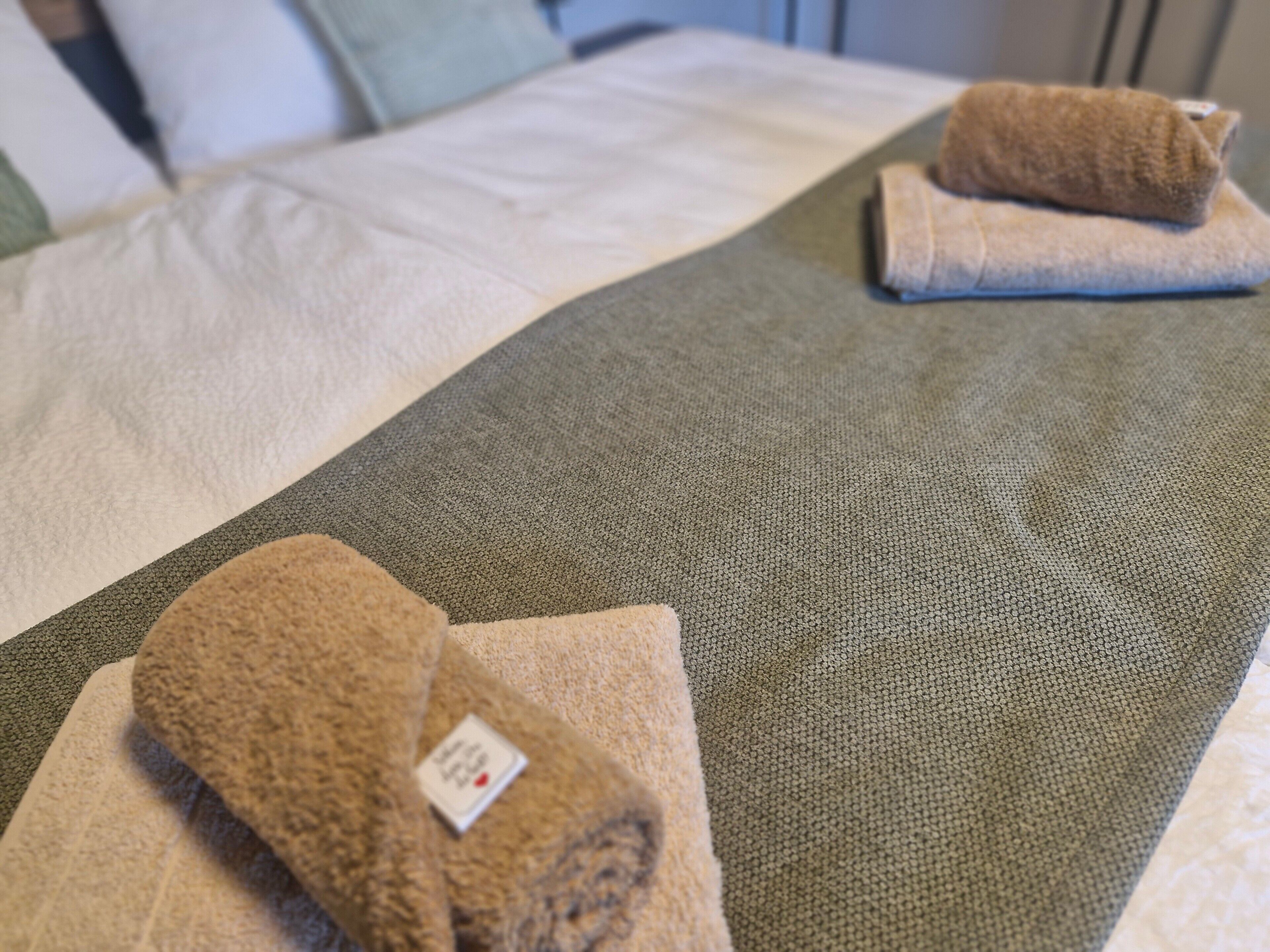 Ein Bett mit einer grau-beigen Decke, einem braunen Handtuch und einem Aufkleber auf dem Handtuch.