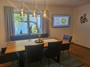 A dining area with a wooden table, black chairs, a vase with flowers, and a framed welcome sign.