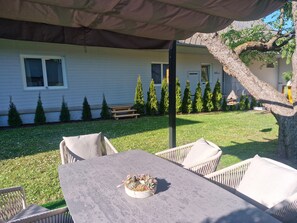 A patio with a table and chairs, a covered area, a lawn, and a house in the background.