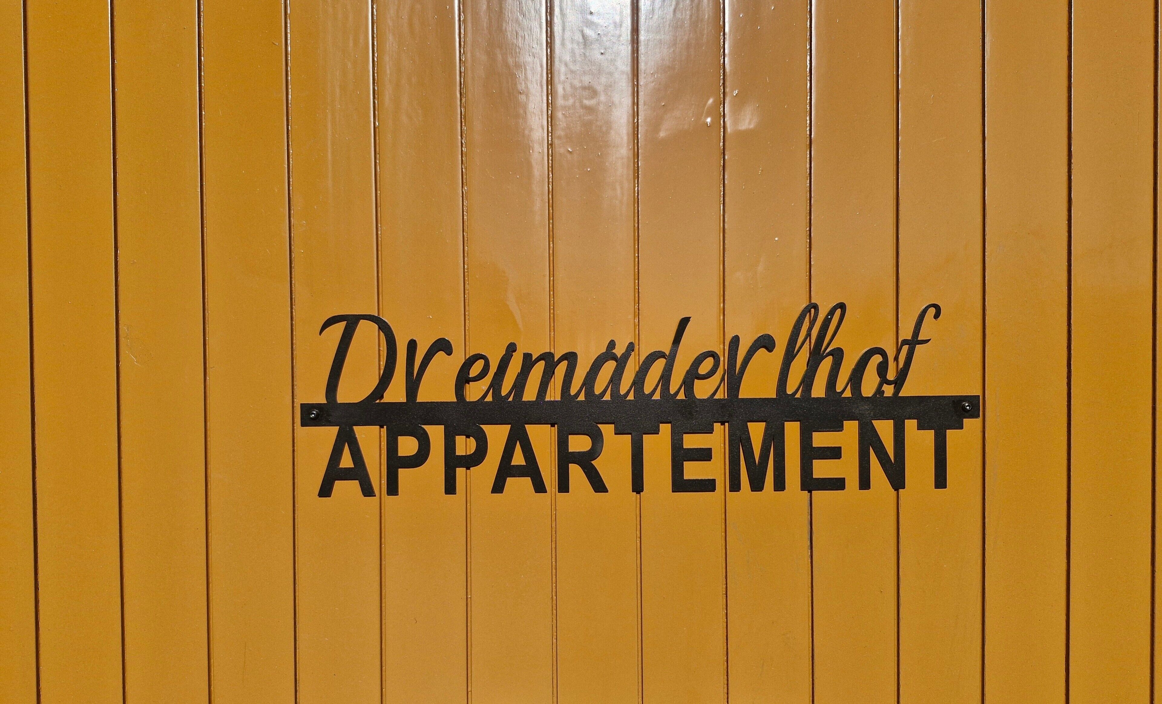 A yellow wall with the text 'Dreimädlerhof APARTMENT' in black.