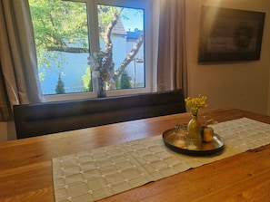 A dining area with a wooden table, a placemat, a vase with yellow flowers, and a certificate on the wall.