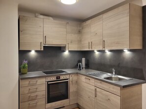 A modern kitchen with wooden cabinets, a built-in oven, a stainless steel sink, and under-cabinet lighting.