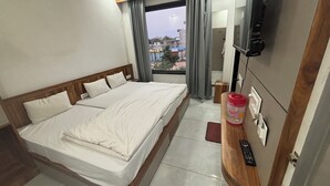 Una habitación de hotel con cama, televisor, control remoto y ventana con cortinas.