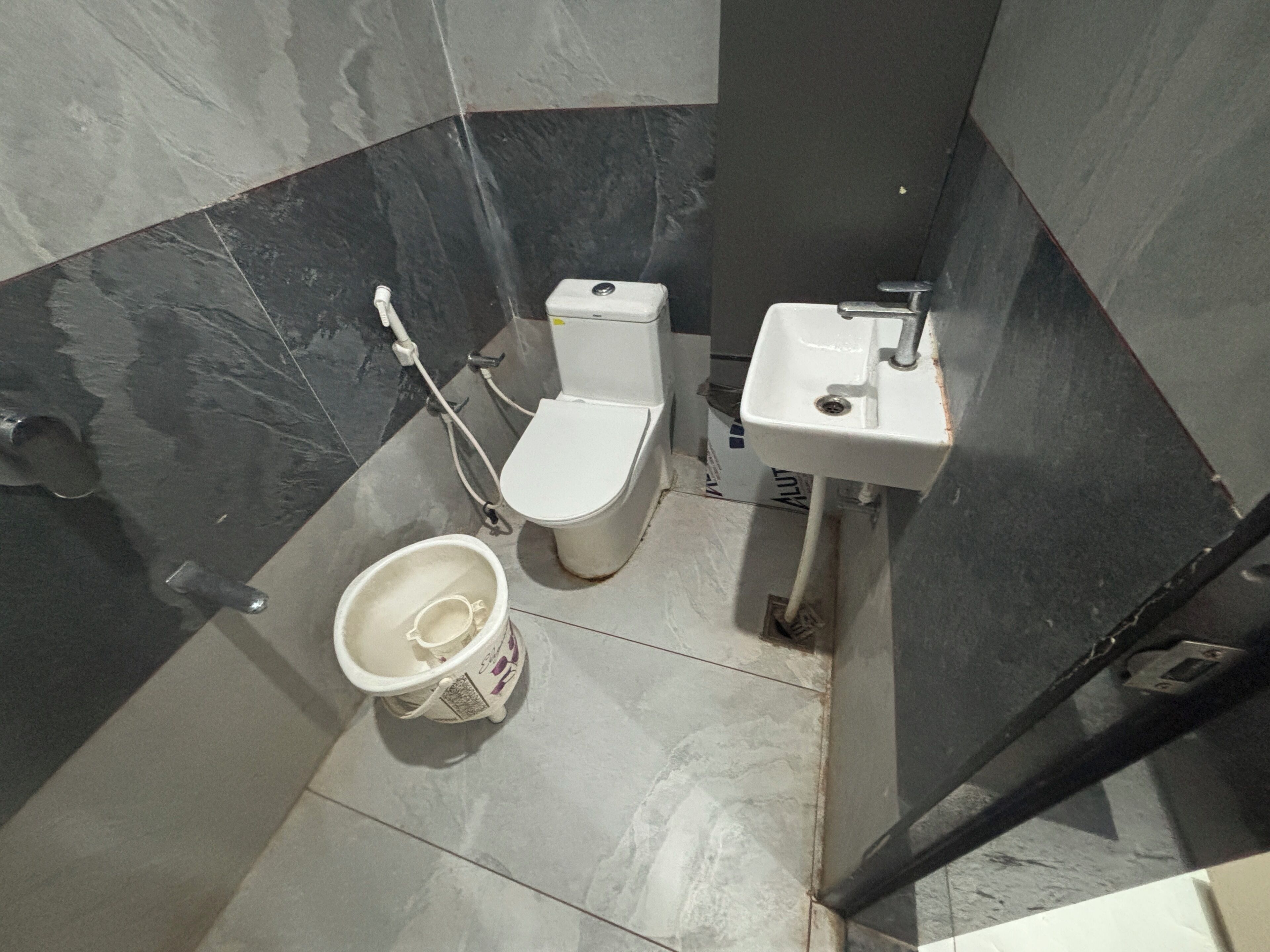 Une salle de bain équipée de toilettes, d’un lavabo et d’un seau.