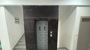Un ascensor con pantalla digital, pared de mármol y suelo de baldosas.