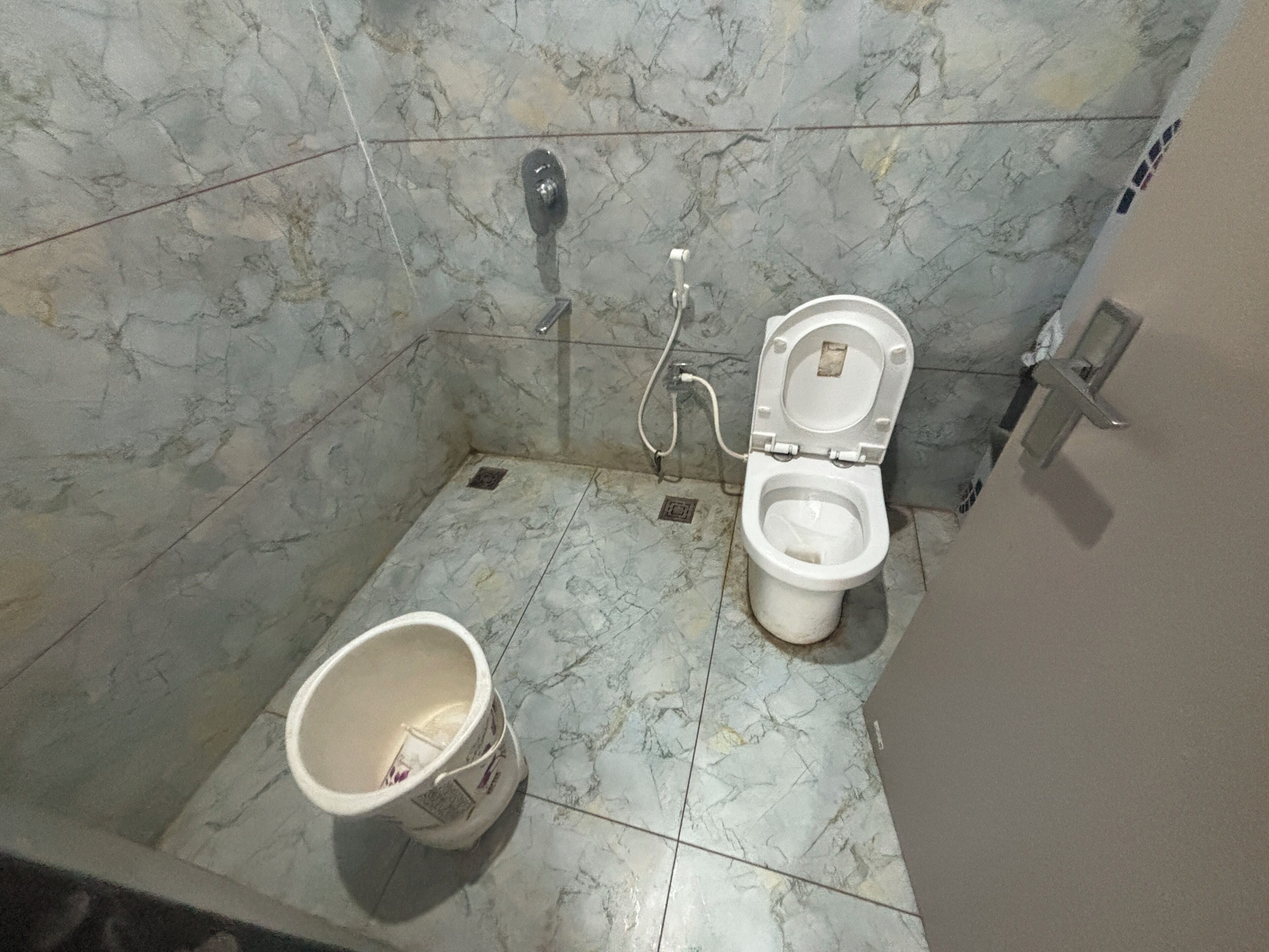 A bathroom with a toilet, a bucket, and marble tiles.