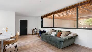 A modern living space with a dining area, a sofa, and a large window.