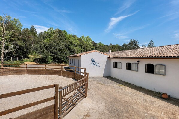 A stable with a wooden fence, a white building with a tiled roof, and a mural of a horse.