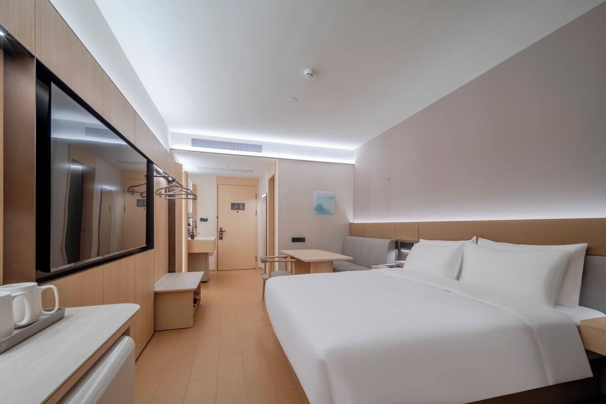 A hotel room with a bed, bedside table, a desk, a chair, a mirror, and a TV.