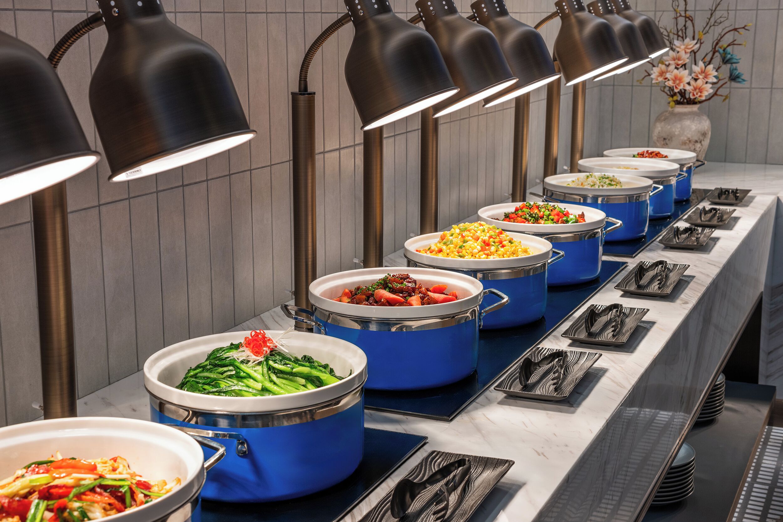 A buffet setup with multiple blue serving containers, black serving trays, and overhead lighting.
