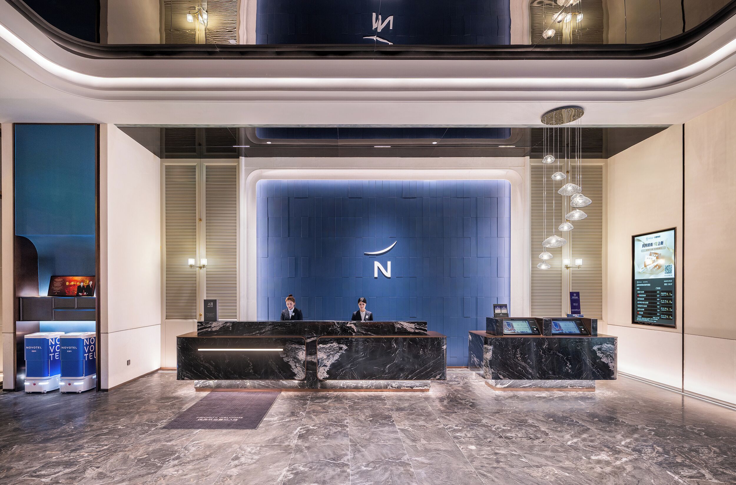 A modern hotel reception area with marble counters, a blue accent wall, and a digital information board.