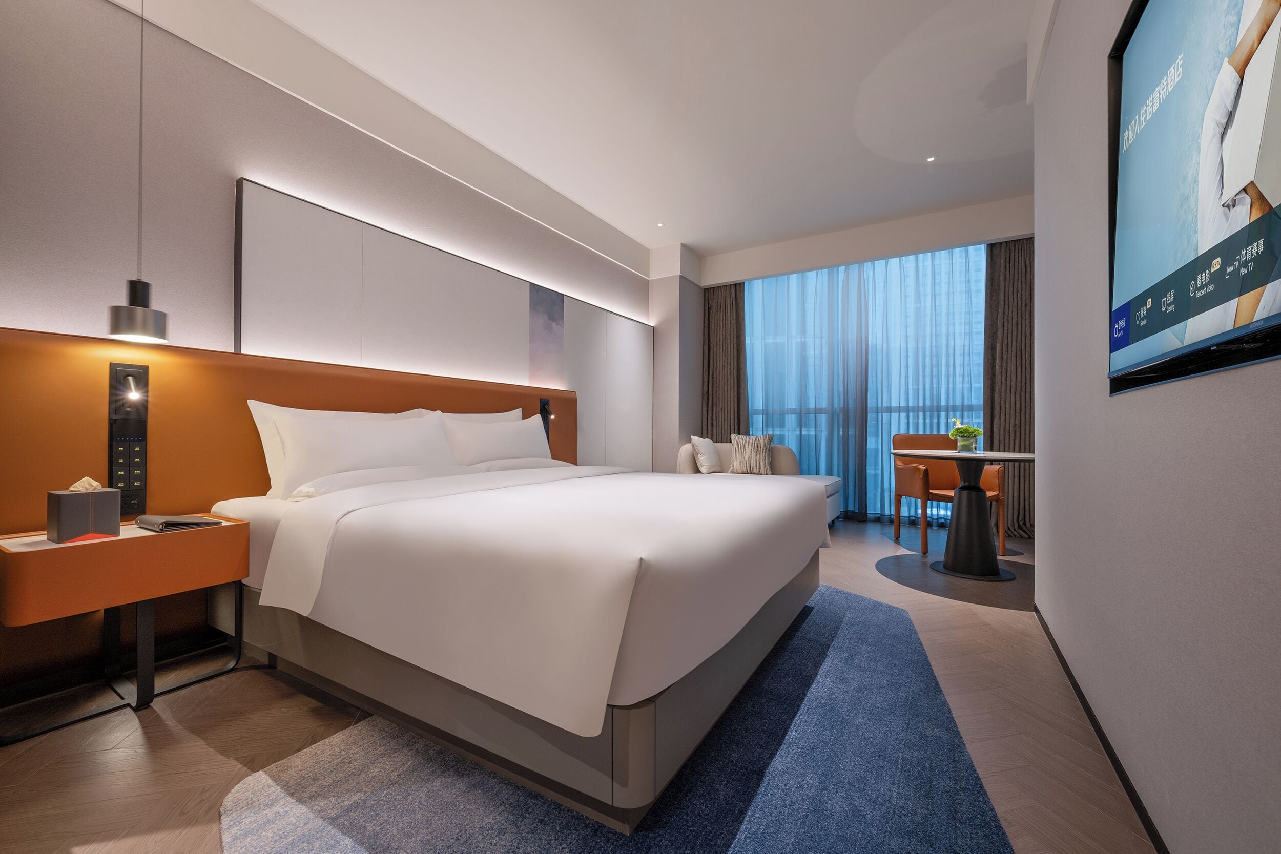 Una habitación de hotel moderna con una cama grande, una mesita de noche con lámpara, un televisor en la pared y un balcón con vistas.