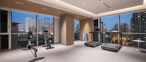 Un gimnasio moderno con equipo de ejercicio, ventanas amplias y vistas a la ciudad.