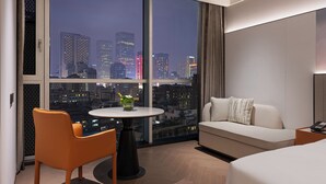 A modern hotel room with a large window, a round table with a vase, a sofa, and a bed. - Novotel Chengdu Chunxi Road (Chengdu)