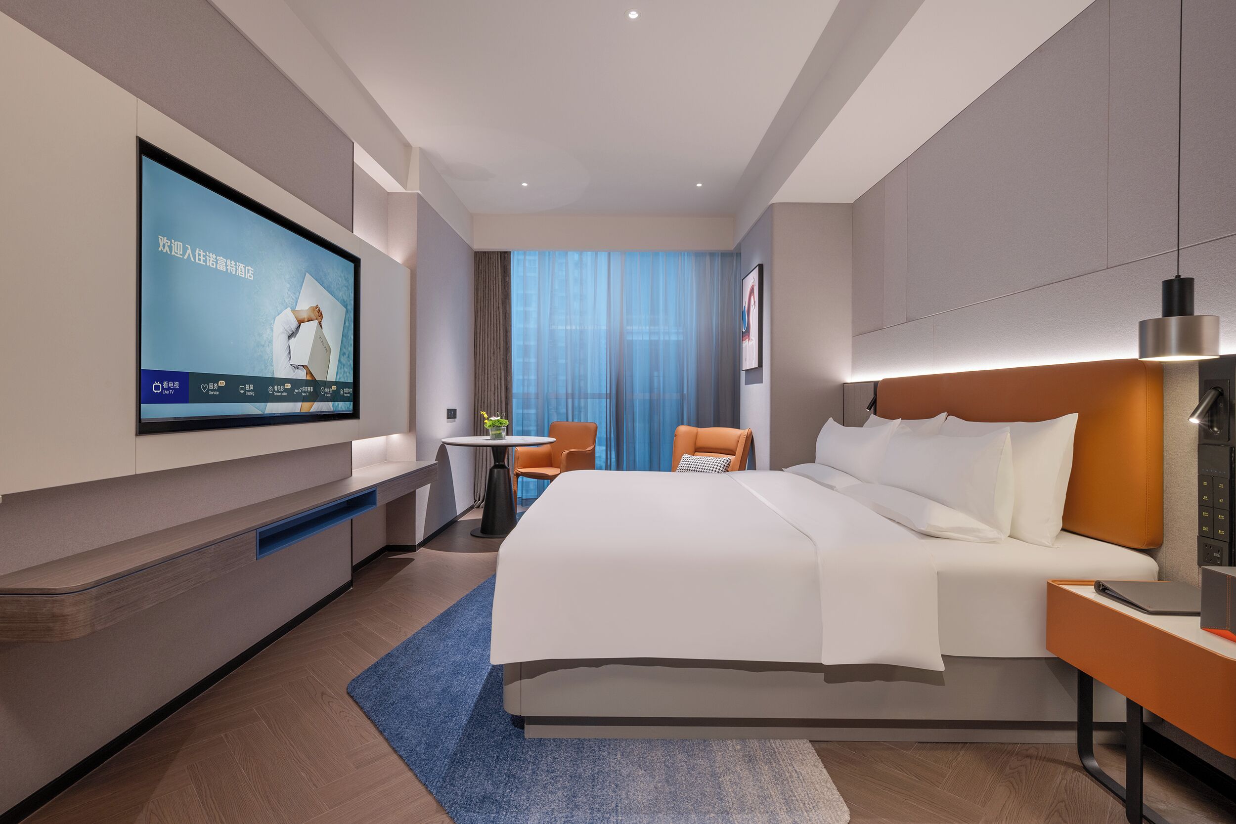 A modern hotel room with a large bed, a desk, a TV mounted on the wall, and a view of the city through the window.