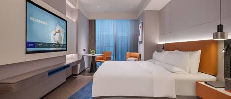 A modern hotel room with a large bed, a desk, a TV mounted on the wall, and a view of the city through the window.
