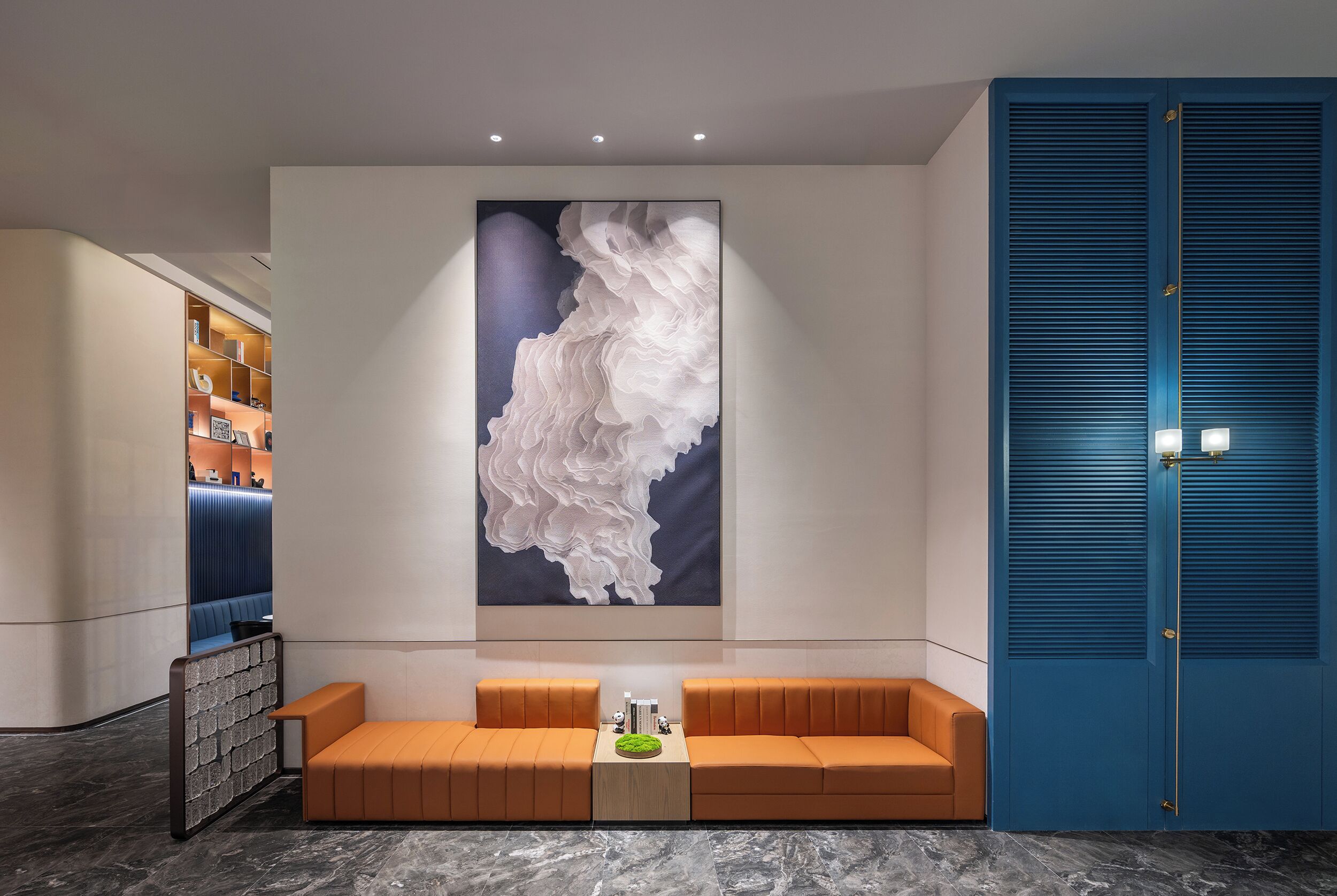 Un lobby moderno con una zona de estar, un cuadro abstracto grande y una puerta azul.