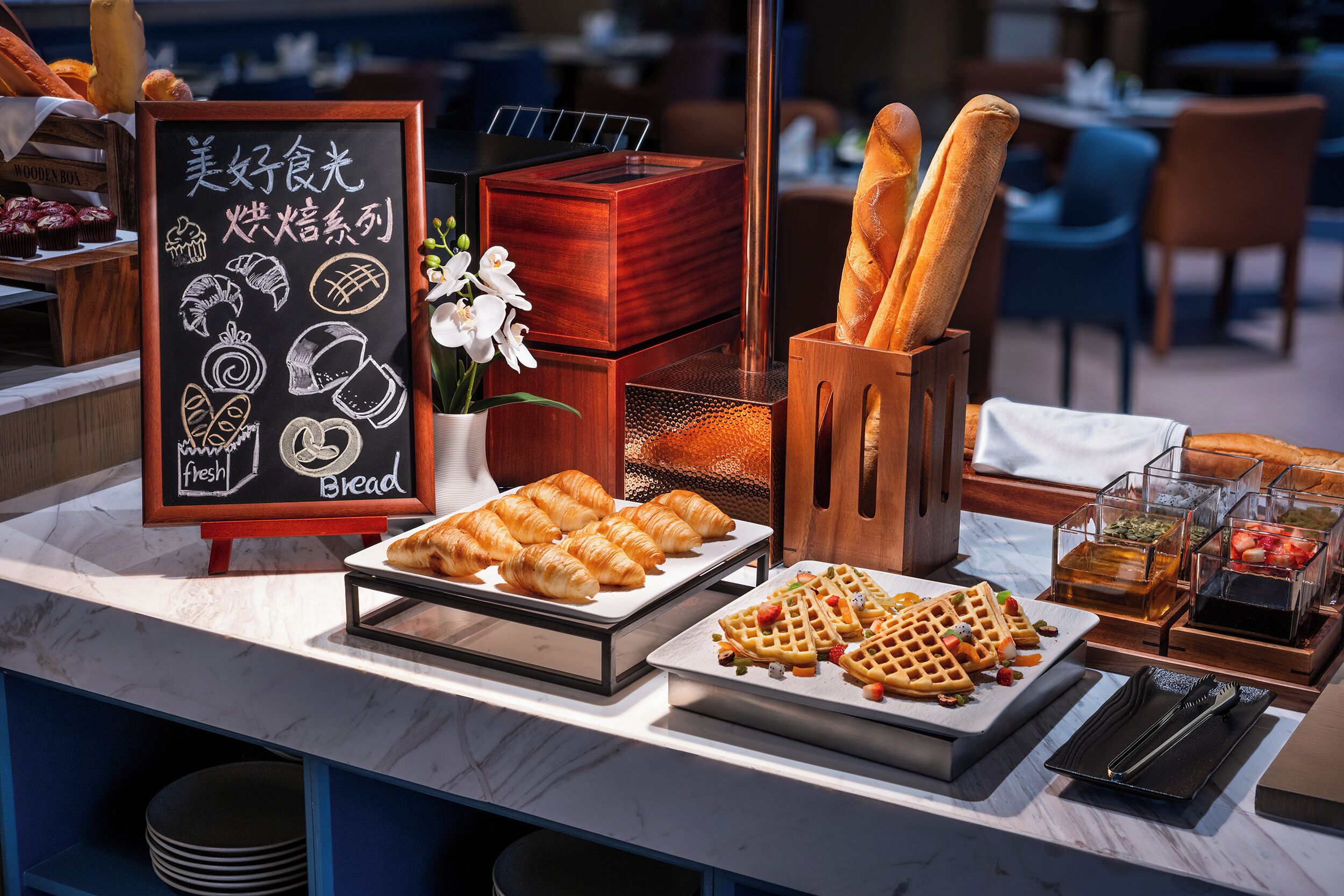 Un buffet de petit-déjeuner comprenant du pain, des viennoiseries, des gaufres et des fruits.