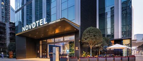 A modern hotel with a prominent 'NOVOTEL' sign, large windows, and a well-lit entrance.