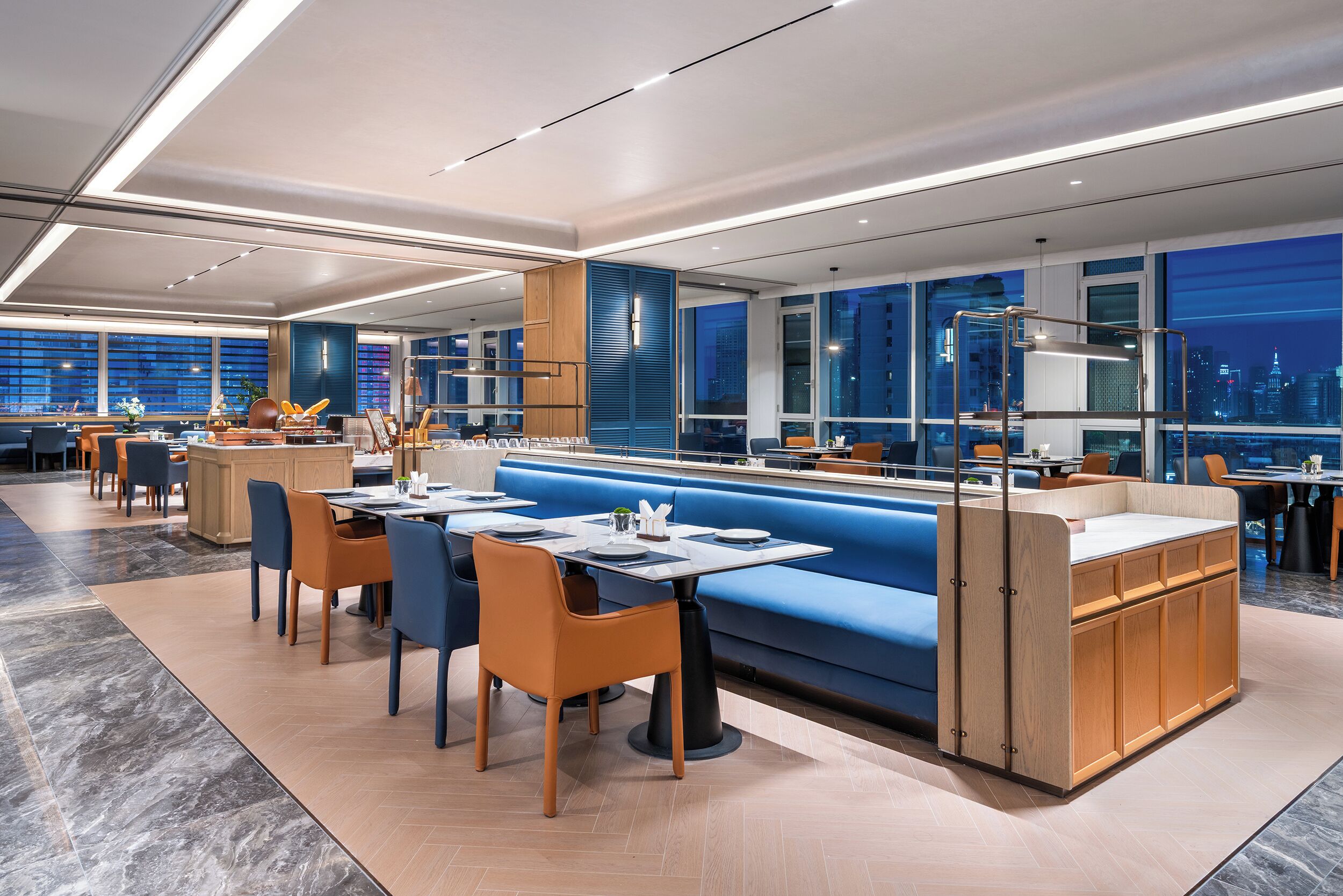 A modern restaurant with a blue booth seating area, wooden cabinets, and a city view.