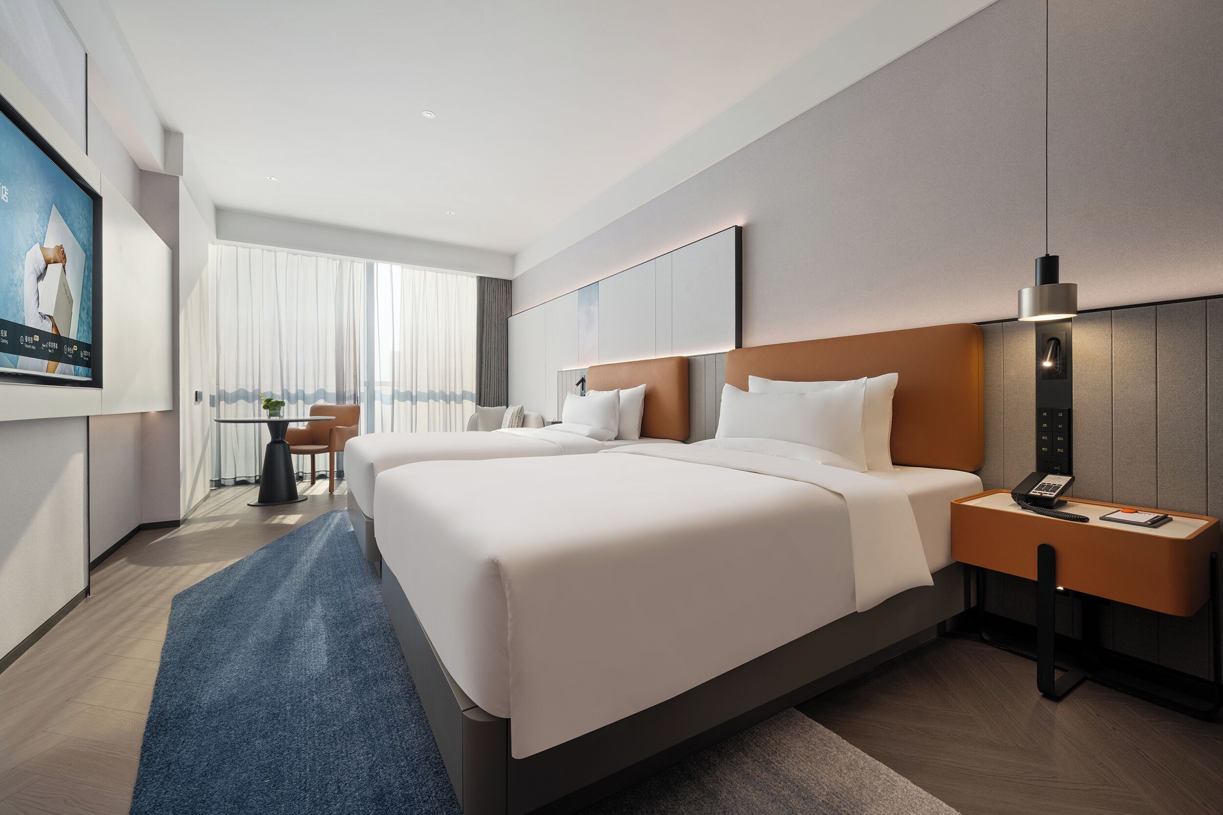 Een hotelkamer met een groot bed, een bureau met telefoon, een stoel en een televisie aan de muur.