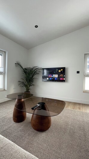 A modern living room with a flat-screen TV mounted on the wall, a glass coffee table, a potted plant, and a remote control on the table. - Modern apartment with balcony & parking space in Söhlde (Söhlde)