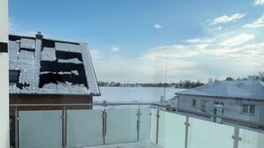 Ein mit Schnee bedeckter Balkon mit freiem Blick auf den Himmel und entfernte Gebäude.