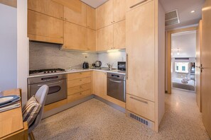 Cocina compacta con armarios de madera, electrodomésticos de acero inoxidable y un comedor con una silla y una mesa.