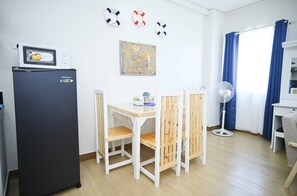 A compact living space with a kitchenette, a dining table with chairs, a map on the wall, and a fan near the window. - Condotel in SM Trece Martires (Trece Martires)