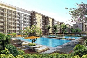 A hotel with a swimming pool, outdoor seating, and lush greenery. - Condotel in SM Trece Martires (Trece Martires)