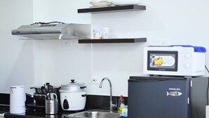 A kitchen with a stove, sink, and a microwave on a stand. - Condotel in SM Trece Martires (Trece Martires)