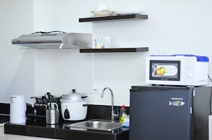 A kitchen with a stove, sink, and a microwave on a stand. - Condotel in SM Trece Martires (Trece Martires)