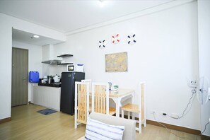 A compact kitchen with a refrigerator, stove, and microwave. There is a dining table with chairs and a small sofa. A map is displayed on the wall. - Condotel in SM Trece Martires (Trece Martires)