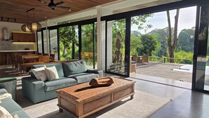 A modern living room with a large sofa, a wooden coffee table, and a dining area with wicker furniture. - Villa Maxwell (Tabanan)