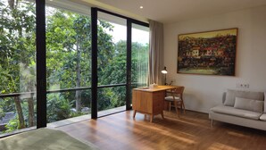 A room with a large window, a desk, a chair, a sofa, and a painting on the wall. - Villa Maxwell (Tabanan)