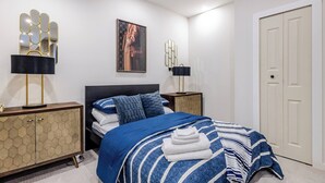 Ein Schlafzimmer mit einem Bett, einem Kleiderschrank, zwei Nachttischen, einem Wandspiegel und einem gerahmten Bild.